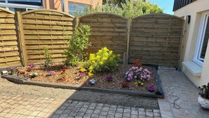 A garden with a wooden fence, various plants, and a tiled patio area. - Charming gîte in Carantec, 44m² of happiness between sea, calm and barbecue! (Carantec)