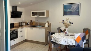 Une cuisine moderne avec des armoires blanches, un four encastré et un four à micro-ondes. On y trouve un coin repas avec une table dressée pour deux personnes, des chaises et un vase rempli de fleurs.