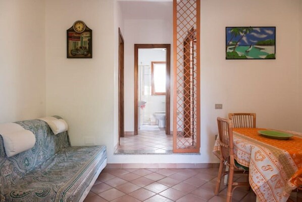 Una habitación con sofá, una mesa de comedor con sillas, un biombo decorativo y un cuadro en la pared.