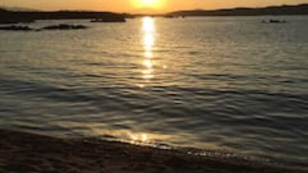 Solnedgang over stille vand med en fjerntliggende kystlinje.