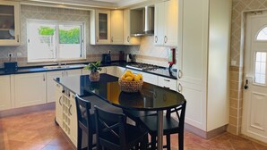 Een moderne keuken met witte kasten, een centraal eiland met stoelen en uitzicht op groen.