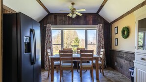 A kitchen with a black refrigerator, wooden dining table with six chairs, a ceiling fan, and a view through large windows. - Dragonfly Cottage-Pet-friendly, relaxing Wellsboro retreat (Charleston Township)