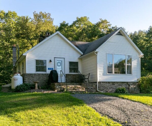 A single-story house with a stone foundation and white siding, a chimney, and a covered grill area. - Dragonfly Cottage-Pet-friendly, relaxing Wellsboro retreat (Charleston Township)