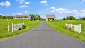A rural road leading to two white houses with a white picket fence on either side.