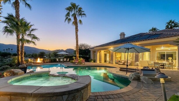 Un área de piscina exterior lujosa con un jacuzzi, rodeada de palmeras y un patio con mobiliario de exterior.