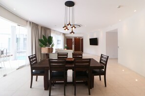A modern dining area with a round table and six chairs, a hanging light fixture, and a large potted plant.