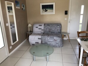 Ein Wohnzimmer mit einer Couch, einem Glastisch, einem kleinen Beistelltisch und einem gerahmten Bild an der Wand.