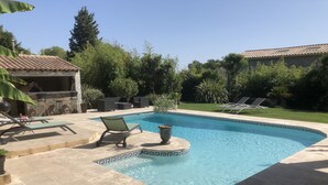 A swimming pool with lounge chairs, a stone barbecue area, and a well-maintained garden. - Studio 20m2 30 minutes from the beach (Saussines)