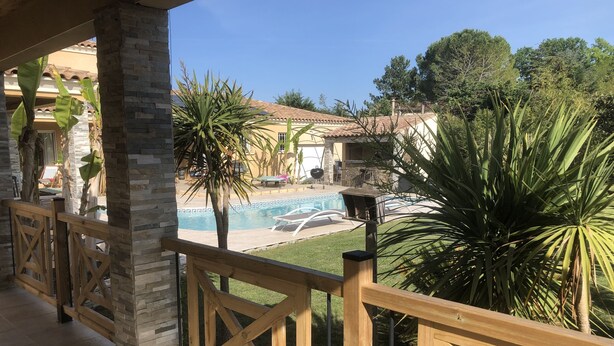 A pool area with a wooden deck, stone pillars, and tropical plants. - Studio 20m2 30 minutes from the beach (Saussines)