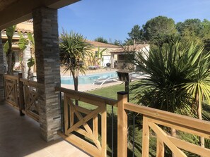 A pool area with a wooden deck, stone pillars, and tropical plants. - Studio 20m2 30 minutes from the beach (Saussines)