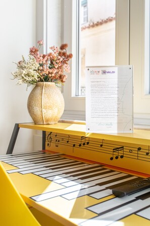 Ein Klavier mit Noten, eine Vase mit Blumen und ein Fenster im Hintergrund.