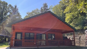 A wooden cabin with a porch, large windows, and a stone wall in the background. - Cozy Cabin get away - walking distant to beach (Crofton)