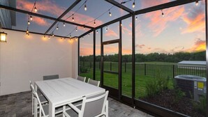 A covered patio with a table and chairs, large windows, and string lights. - Exclusive at Reunion Golf View Resort Style 764 (Celebration)