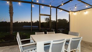 Un espace extérieur abrité, aménagé pour les repas, avec une table et des chaises, des guirlandes lumineuses et une vue sur le paysage environnant.