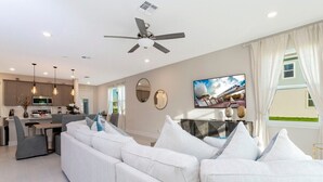 Un salon moderne comprenant un canapé, un coin repas, une cuisine et un téléviseur fixé au mur.