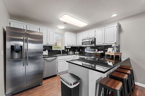 Une cuisine moderne dotée d’appareils électroménagers en acier inoxydable, de meubles blancs et d’un îlot central avec des tabourets.