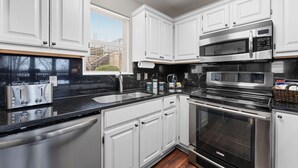 A modern kitchen with white cabinets, stainless steel appliances, a black countertop, and a window with blinds. - Spacious remodel 5 mn-SDC, 10 mn-Lake, 2BR 2.5BA (Branson West)