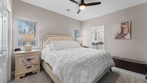 A bedroom with a bed, bedside tables, a ceiling fan, a window with blinds, a mirror, and a painting on the wall. - Spacious remodel 5 mn-SDC, 10 mn-Lake, 2BR 2.5BA (Branson West)