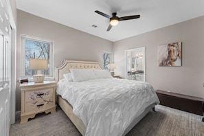 A bedroom with a bed, bedside tables, a ceiling fan, a window with blinds, a mirror, and a painting on the wall. - Spacious remodel 5 mn-SDC, 10 mn-Lake, 2BR 2.5BA (Branson West)
