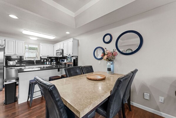 A modern kitchen with white cabinets, a central island, and a dining area with a marble table and black chairs.