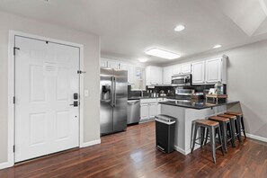 A modern kitchen with stainless steel appliances, white cabinetry, and a wooden island with bar stools. - Spacious remodel 5 mn-SDC, 10 mn-Lake, 2BR 2.5BA (Branson West)