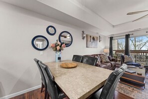 Un coin repas avec une table en marbre, des chaises en cuir et un vase rempli de fleurs. On y trouve également trois miroirs fixés au mur et un tableau représentant des chevaux.