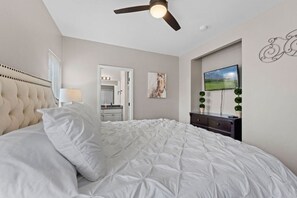 A bedroom with a tufted headboard, a large bed with white bedding, a ceiling fan, a TV mounted on the wall, and a door leading to a bathroom. - Spacious remodel 5 mn-SDC, 10 mn-Lake, 2BR 2.5BA (Branson West)