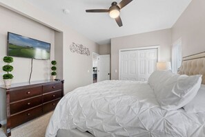 A bedroom with a bed, dresser, ceiling fan, and a painting on the wall.