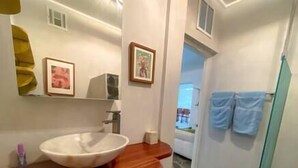 A bathroom with a large white sink, wooden countertop, and a small mirror. There are two framed pictures on the wall and a towel rack with two towels.