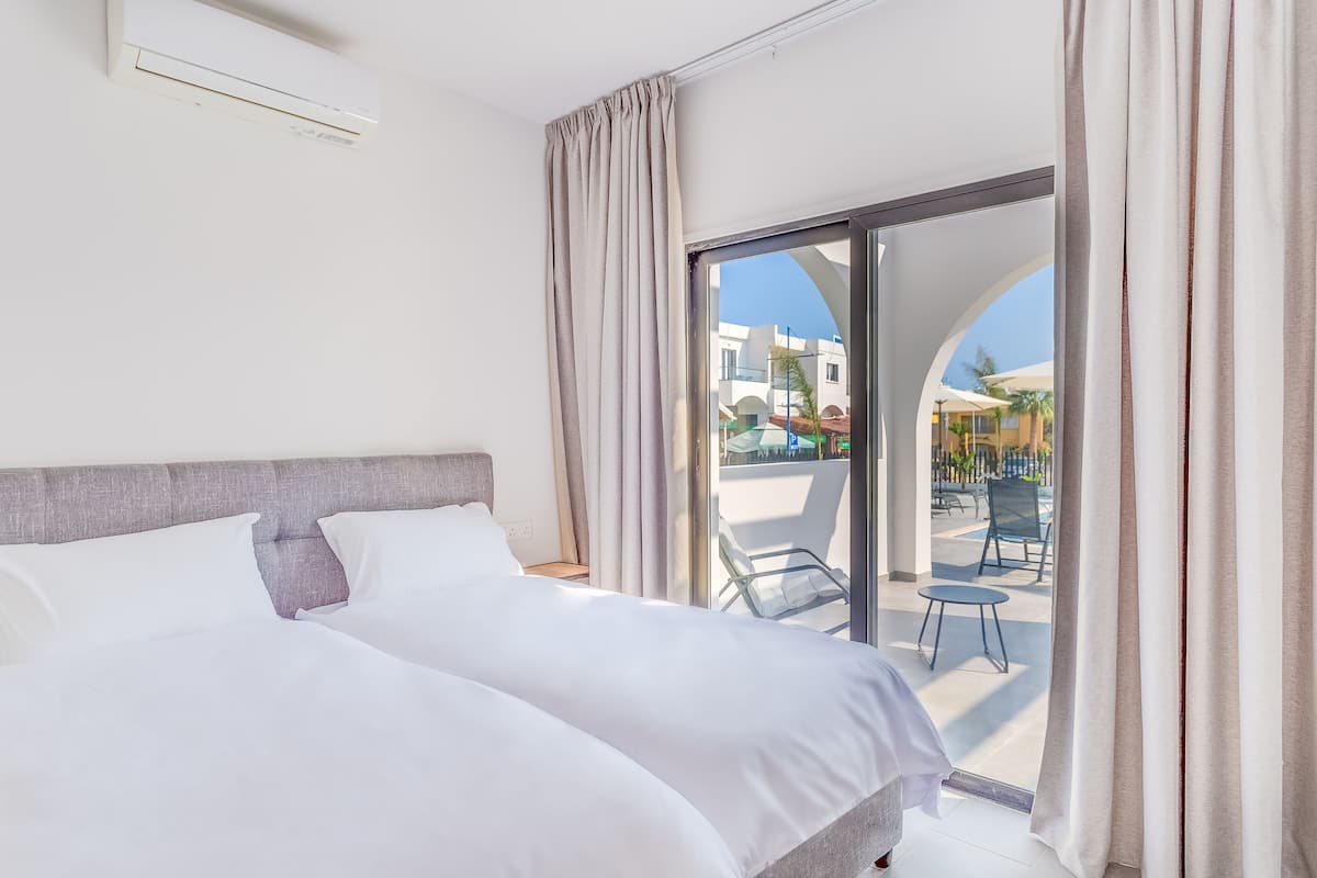 A hotel room with a bed, a window with curtains, and a view of the outside.