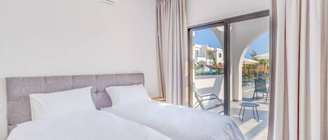 A hotel room with a bed, a window with curtains, and a view of the outside.