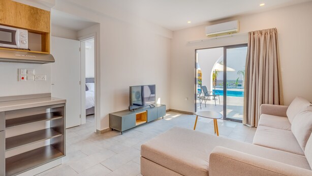 A modern living room with a sofa, TV, and a view of a pool. - Zoi ayia Napa hotel (Ayia Napa)