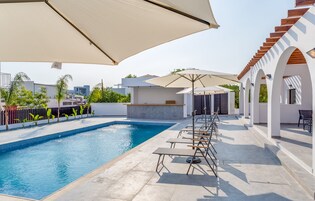 Piscina com espreguiçadeiras e guarda-sóis, num ambiente arquitetónico moderno.