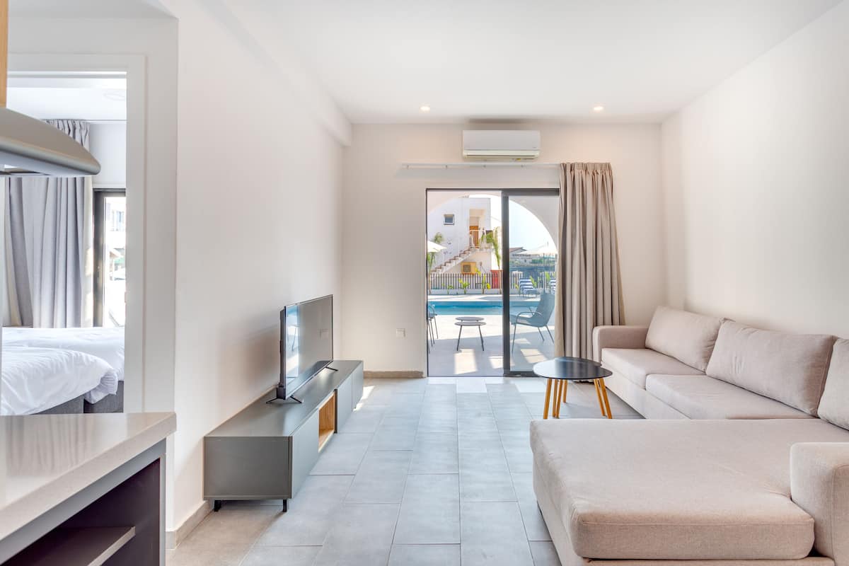 A modern hotel room with a bed, a TV, a sofa, and a balcony with a pool view.