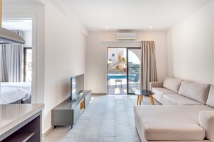 Una habitación de hotel moderna con cama, televisor, sofá y balcón con vista a la piscina.