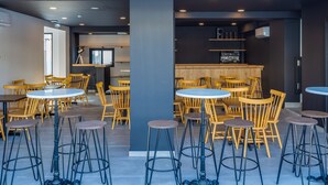 A modern interior with round tables and wooden chairs, a bar area, and a staircase leading to an upper level. - Zoi ayia Napa hotel (Ayia Napa)