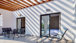 A modern outdoor patio with a wooden pergola, a glass door leading to a room, and a seating area with chairs and a table. - Zoi ayia Napa hotel (Ayia Napa)
