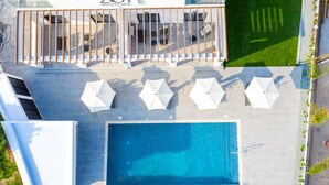 An aerial view of a rooftop pool area with a rectangular pool, white umbrellas, and lounge chairs. - Zoi ayia Napa hotel (Ayia Napa)