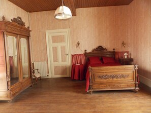 Une chambre avec un lit en bois, un grand miroir, une armoire en bois et un luminaire suspendu.