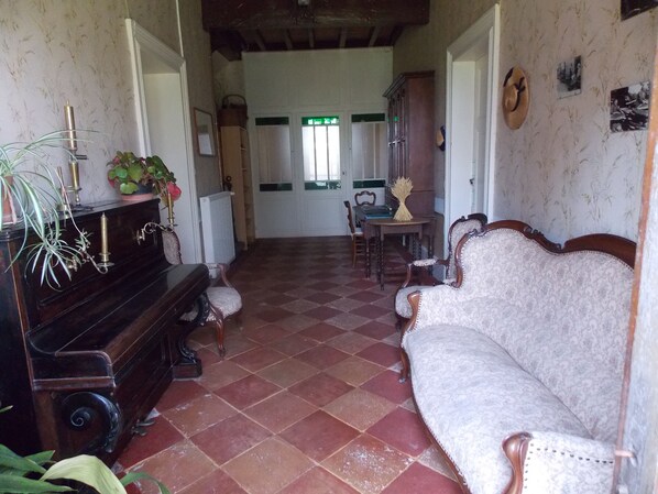 Una habitación con piano, sofá, mesa de comedor y radiador.