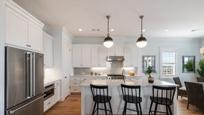A modern kitchen with white cabinetry, stainless steel appliances, and a central island with bar stools.