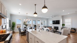A spacious kitchen with a large island, white cabinetry, and a built-in stove. There are multiple windows providing natural light and a view of the outdoors.