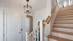A staircase with wooden steps and white railings, leading to a landing with a door and a hanging light fixture.