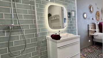 Un baño moderno con cabina de ducha de vidrio, un tocador blanco con espejo y suelo estampado.
