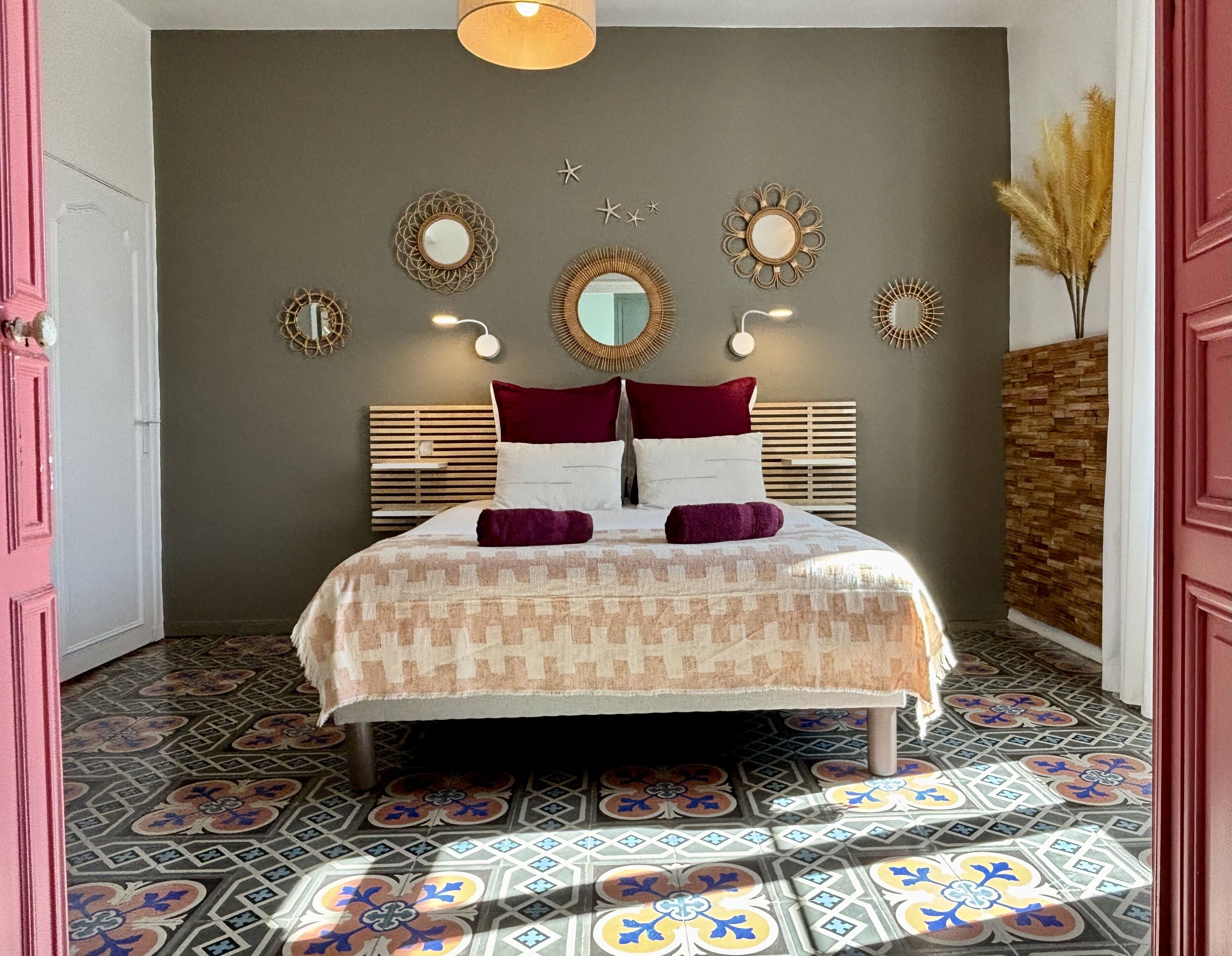 Un dormitorio con suelo estampado, una cama con colcha estampada, cabecero y espejos montados en la pared.