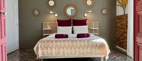 A bedroom with a patterned floor, a bed with a patterned bedspread, a headboard, and wall-mounted mirrors.