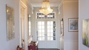 A hallway with patterned floor tiles, a white radiator, a wooden table with decorative items, a chandelier, and a door with glass panels. - Casa Belle (Sérignan)
