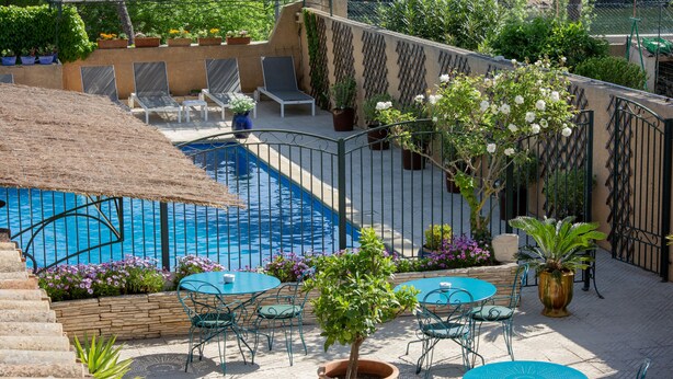 A pool area with a thatched roof, lounge chairs, and a small tree. - Casa Belle (Sérignan)