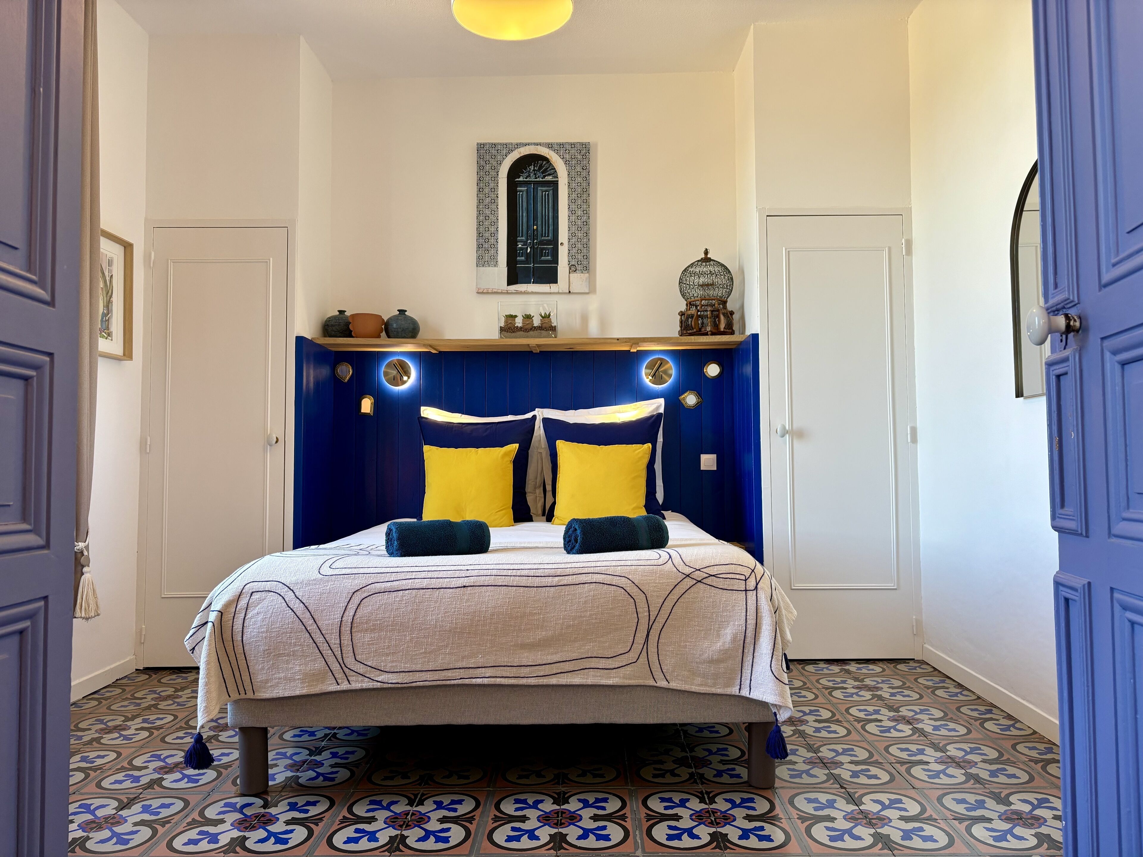 A bedroom with a bed, a wooden headboard, a wall-mounted shelf, and a decorative mirror.