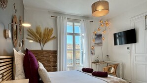 A bedroom with a bed, a TV, a window, and a wall-mounted light fixture. - Casa Belle (Sérignan)